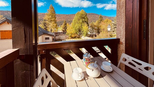 Une terrasse en bois avec une table dressée pour le thé, offrant une vue sur un paysage montagneux aux arbres aux couleurs automnales.