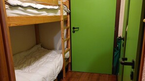 Une chambre avec un lit superposé, une porte verte et un petit tapis sur le sol.