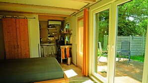 A bedroom with a bed, a small table, and a sliding glass door leading to a patio with a chair and a table. - Vacation between nature and design (Ribnitz-Damgarten)