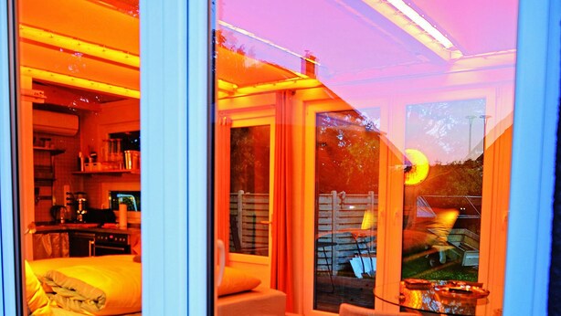 A modern interior with a bed, a chair, and a kitchen area visible through a glass door. - Vacation between nature and design (Ribnitz-Damgarten)