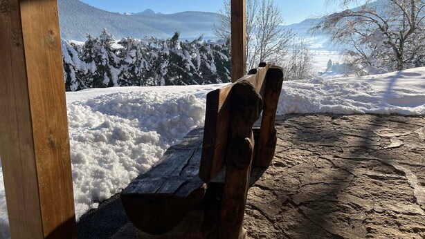 A wooden bench under a shelter with a view of snow-covered mountains and trees.