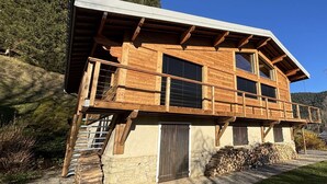 A wooden cabin with a stone foundation, a balcony, and a large window.