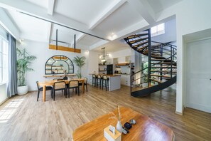 Una cocina moderna con una isla central, un área de comedor con mesa y sillas de madera, y una escalera de caracol que lleva a un nivel superior.