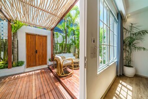 Terraza de madera con un sofá de mimbre y una planta en maceta cerca de una ventana.