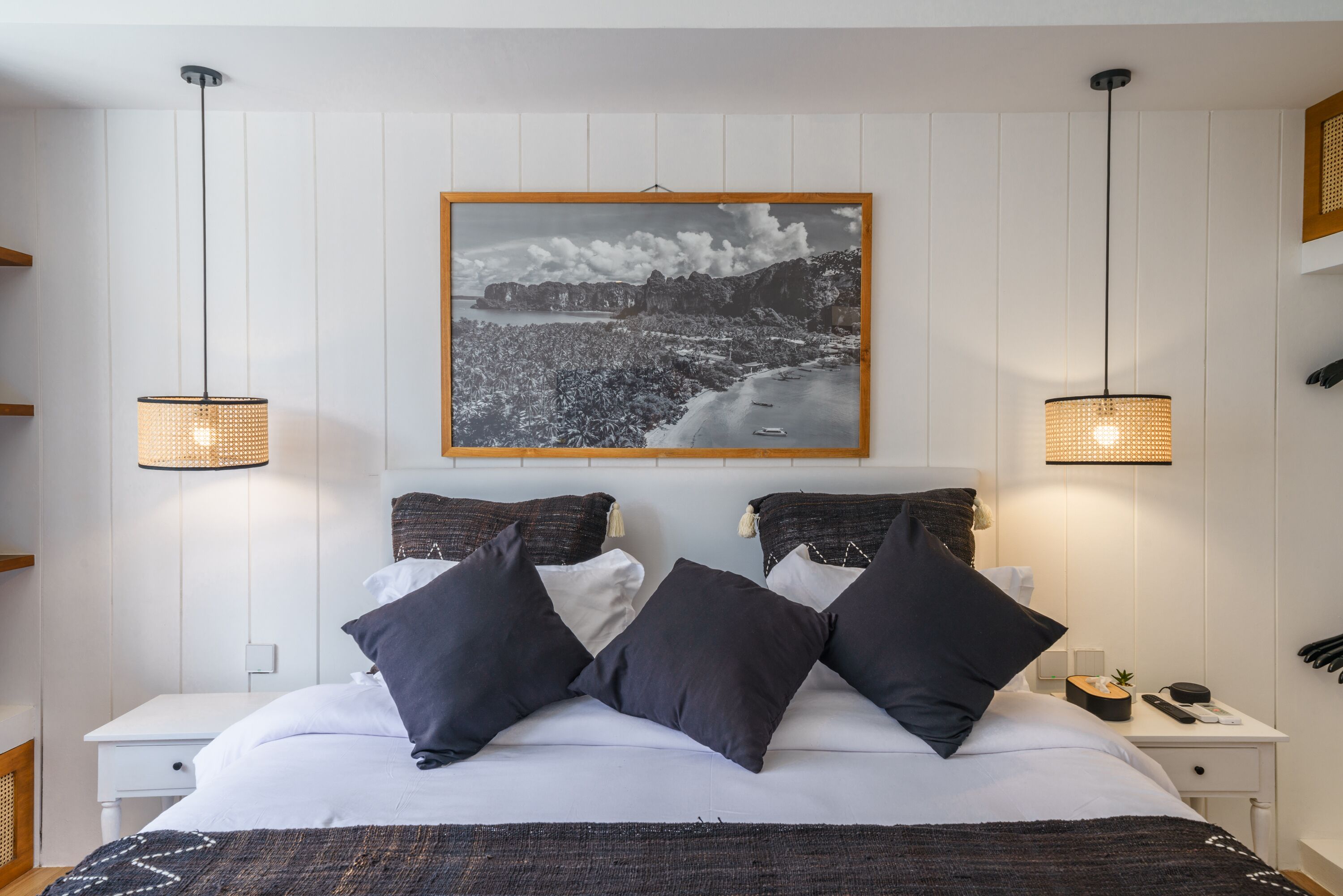 A neatly arranged bedroom with a large bed, two bedside tables, a nightstand, and a wall-mounted picture.