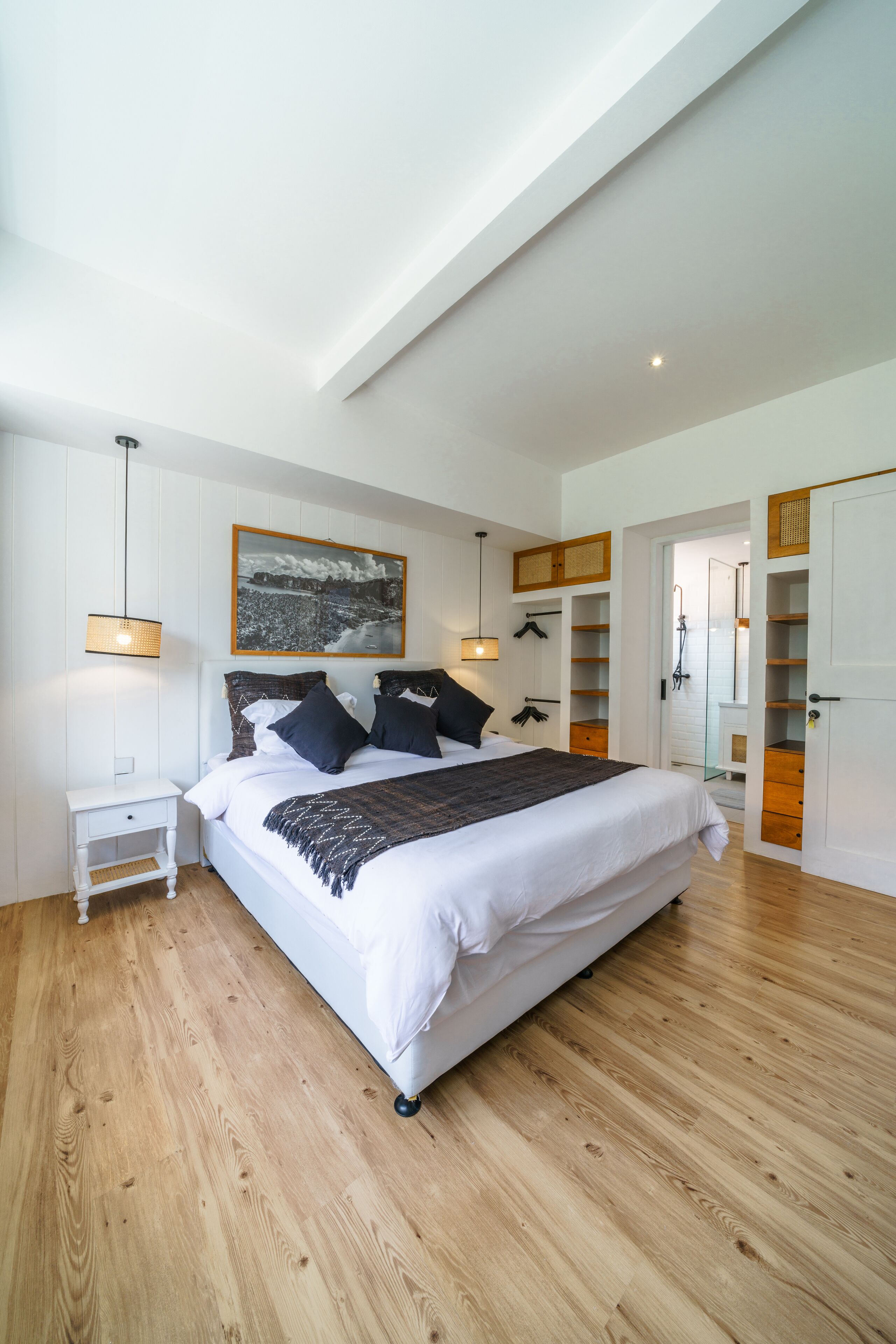 A bedroom with a large bed, a bedside table, a hanging lamp, a framed picture on the wall, and a wardrobe.