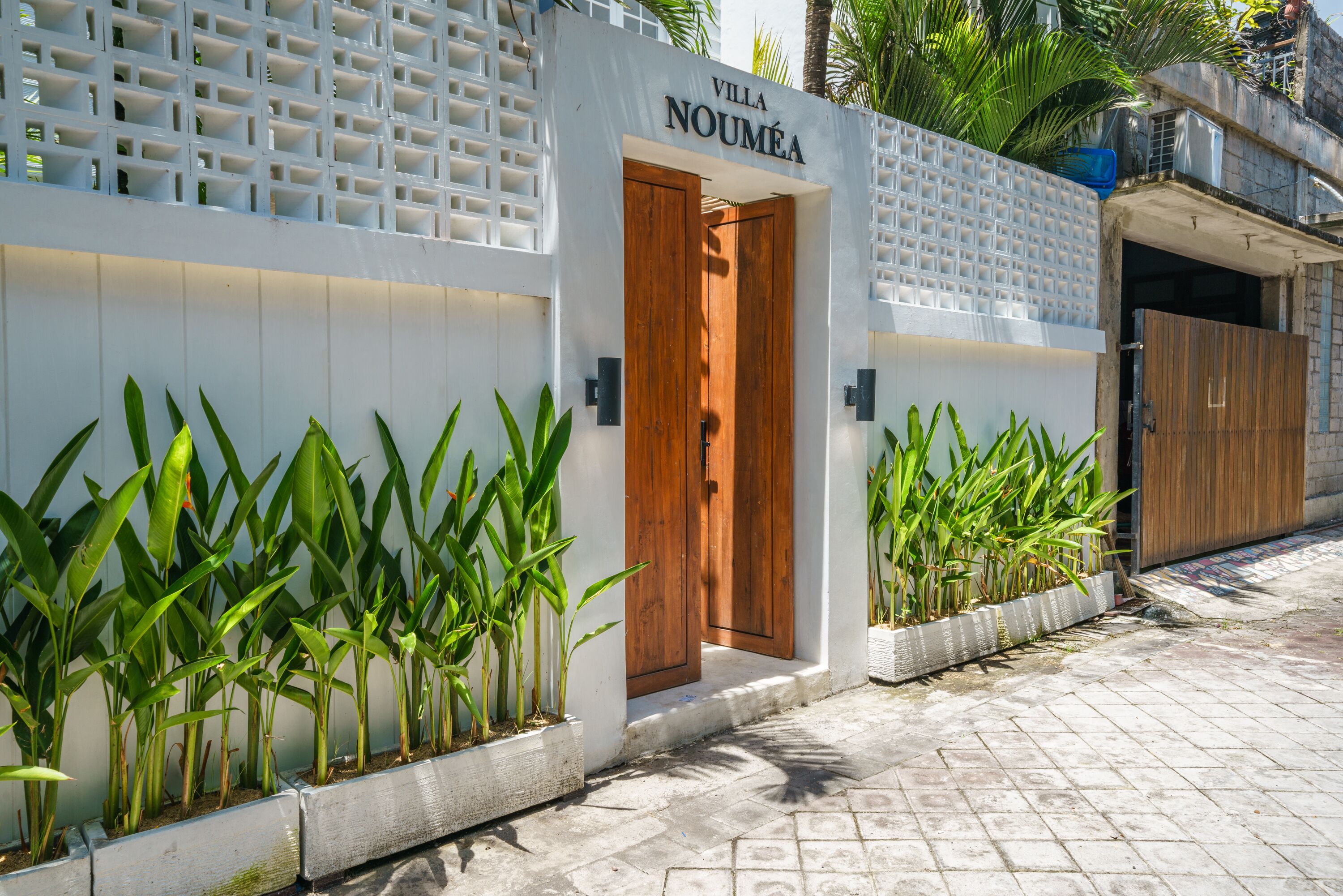 A villa entrance with a wooden door, white walls, and potted plants.