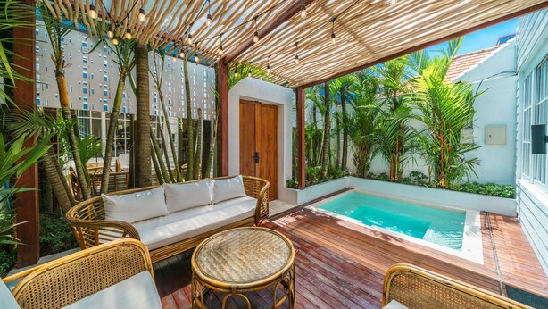 Área à beira da piscina com deck de madeira, móveis de vime e vista para a piscina.