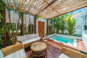 Un área junto a la piscina con terraza de madera, mobiliario de mimbre y vistas a la pileta.