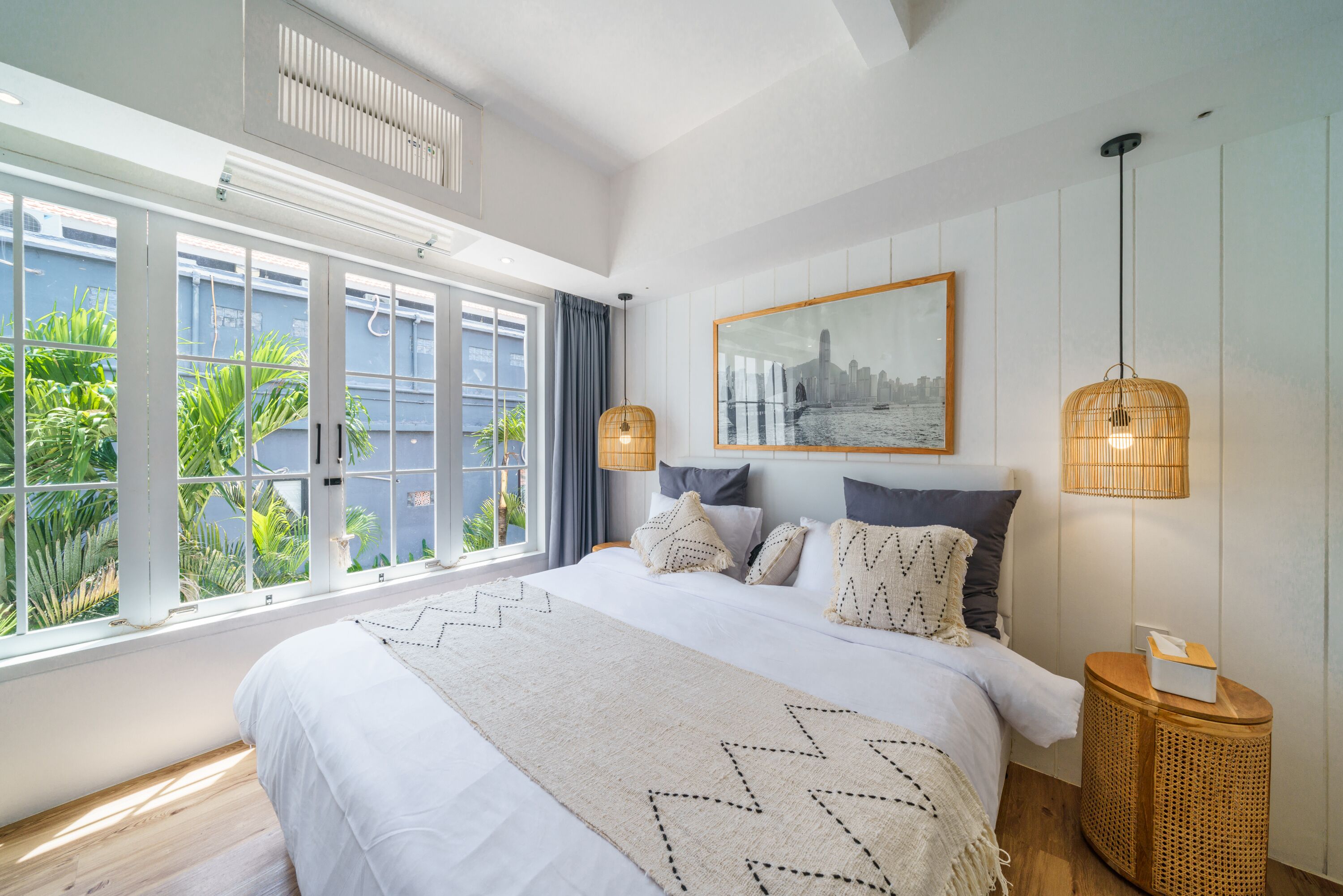 Un dormitorio amplio con una cama grande, un cuadro de paisaje urbano y vistas a zonas verdes por la ventana.