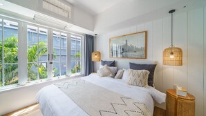 Quarto espaçoso com uma cama grande, uma pintura de paisagem urbana e vista para o verde pela janela.