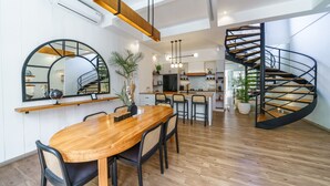Uma cozinha moderna com uma ilha central, uma área de refeições com mesa e cadeiras de madeira, e uma escadaria em espiral.