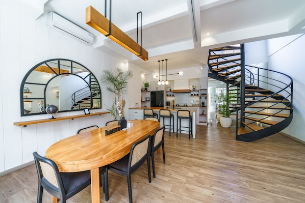 Una cocina moderna con una isla central, un comedor con mesa y sillas de madera, y una escalera de caracol.