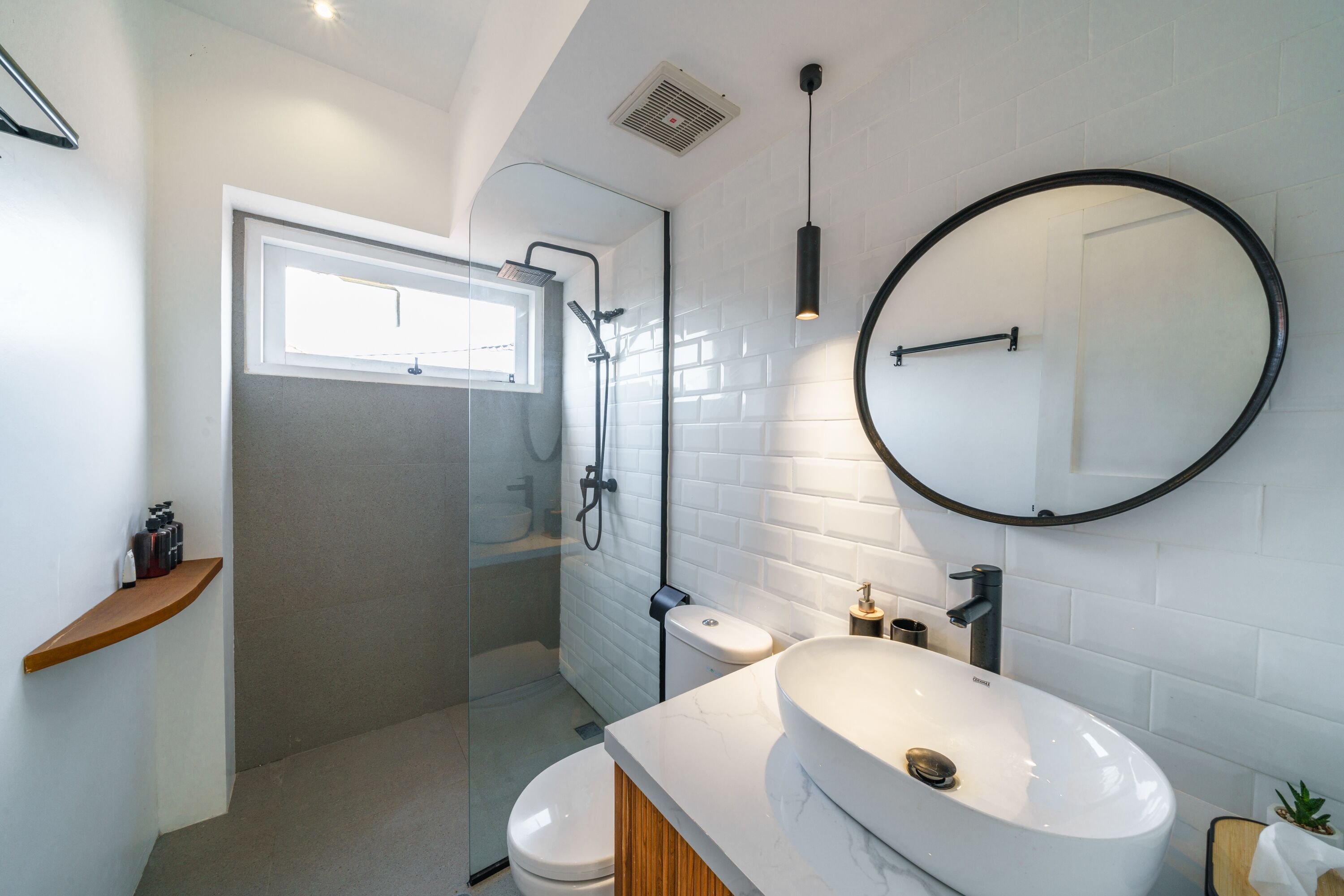 A modern bathroom with a glass shower enclosure, a white sink, and a round mirror.