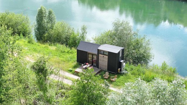 Una cabana moderna amb terrassa, envoltada de verdor abundant i un llac.