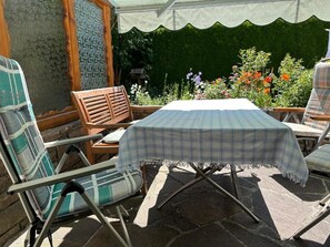 An outdoor patio with a table covered by a plaid tablecloth, surrounded by metal-framed chairs with cushions. - Abendfrieden Vacation Home: 90 m², with a bedroom, bathroom, kitchen, and living room (Mittenwald)