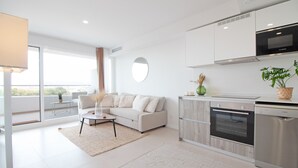 Una cocina moderna con armarios blancos, un horno Bosch y un lavavajillas. Hay un sofá beige con un espejo redondo encima, y una mesa de comedor con sillas.