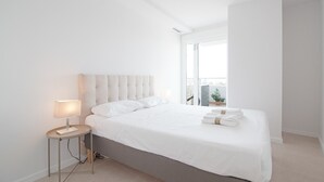 Un dormitorio moderno con una cama grande, una mesita de noche con lámpara y vistas al exterior a través de un amplio ventanal.