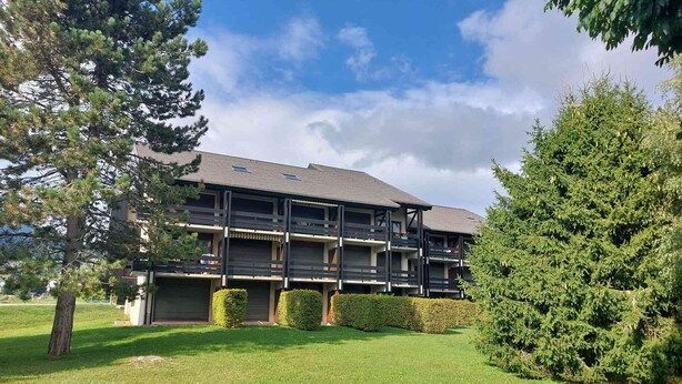 A multi-story building with balconies, surrounded by well-maintained grass and trees.