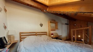 A cozy bedroom with a wooden headboard, a bedside table with a lamp, and a small shelf with decorative items.