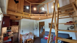 A rustic cabin interior with a loft bedroom, a dining area, and a kitchen.