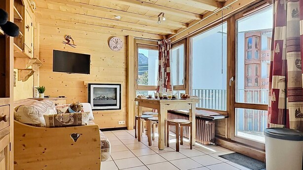 A cozy wooden cabin interior with a dining area, a fireplace, and large windows offering a view of the outside. - 2-room Apartment in Tignes - 4 people (Tignes-Le Lavachet)