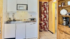 A compact kitchen with white cabinets, a microwave, a sink, and a stove. There is a patterned curtain in the doorway. - 2-room Apartment in Tignes - 4 people (Tignes-Le Lavachet)