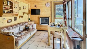 A cozy wooden cabin interior with a sofa, a dining table, and a large window. - 2-room Apartment in Tignes - 4 people (Tignes-Le Lavachet)