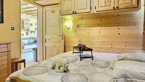 A room with wooden paneling, a bed with a polar bear figurine, a small table with a lamp, and a door leading to another room. - 2-room Apartment in Tignes - 4 people (Tignes-Le Lavachet)