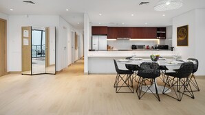 A modern kitchen with white cabinets, a stainless steel refrigerator, and a dining area with a round table and black chairs. - Maison Privee - Stunning Waterfront Apt w/ Open Sea Vws in La Mer (Dubai)
