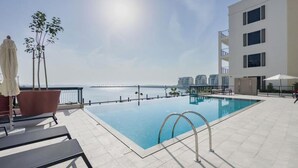 A rooftop pool with a view of the sea and buildings in the background. - Maison Privee - Stunning Waterfront Apt w/ Open Sea Vws in La Mer (Dubai)