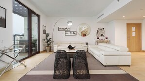 A modern living room with a white sofa, two black woven ottomans, a glass coffee table, and a large mirror on the wall. - Maison Privee - Stunning Waterfront Apt w/ Open Sea Vws in La Mer (Dubai)