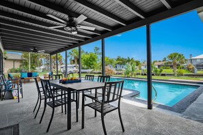 Une terrasse extérieure avec une piscine, un coin repas et des ventilateurs de plafond.