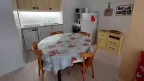 A compact kitchen with a dining table, wooden chairs, a refrigerator, a microwave, and a small cabinet. - Apartment 6 ppl, south balcony, near cross-country ski slopes (Autrans-Méaudre en Vercors-Autrans)