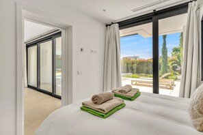 A bedroom with a bed, two towels, a window, and a view of a patio. - Villa Alejandra (Benahavís)