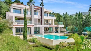 A modern multi-story house with a swimming pool, surrounded by lush greenery and palm trees. - Villa Alejandra (Benahavís)