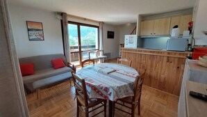 A cozy living area with a dining table, wooden chairs, a sofa, and a kitchen area with cabinets and appliances. - Beautiful duplex for 6, slopeside with parking (Autrans-Méaudre en Vercors-Autrans)