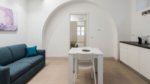 Eine moderne Küche mit weißen Schränken, einem Esstisch und einer Couch mit türkisfarbenen Kissen.