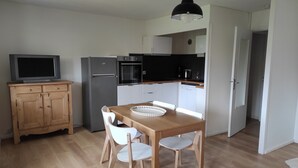 A compact kitchen with a wooden table, white chairs, a black pendant light, a refrigerator, an oven, and a dishwasher. - Charming renovated apartment 47m², 4 pers, near slopes, parking, WiFi (Autrans-Méaudre en Vercors-Autrans)