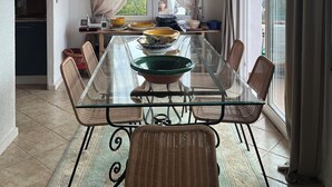 Zona pranzo con tavolo in vetro, sedie in vimini, un lampadario e vista panoramica attraverso ampie finestre.