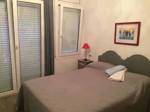 A bedroom with a bed, a nightstand, a lamp, a window with blinds, and a framed picture on the wall. - Villa Panoramique sur Baie de Roses Cap Creus (El Mas Fumats)