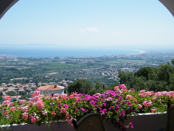 A balcony with a view of a coastal town, a chair, and blooming flowers. - Villa Panoramique sur Baie de Roses Cap Creus (El Mas Fumats)