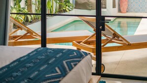 Una habitación con una cama, vista a una piscina y plantas tropicales.