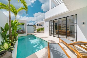 A modern pool area with a clear blue pool, surrounded by lush greenery and a glass-enclosed dining area. - Villa Casa Brezza (Kerobokan)