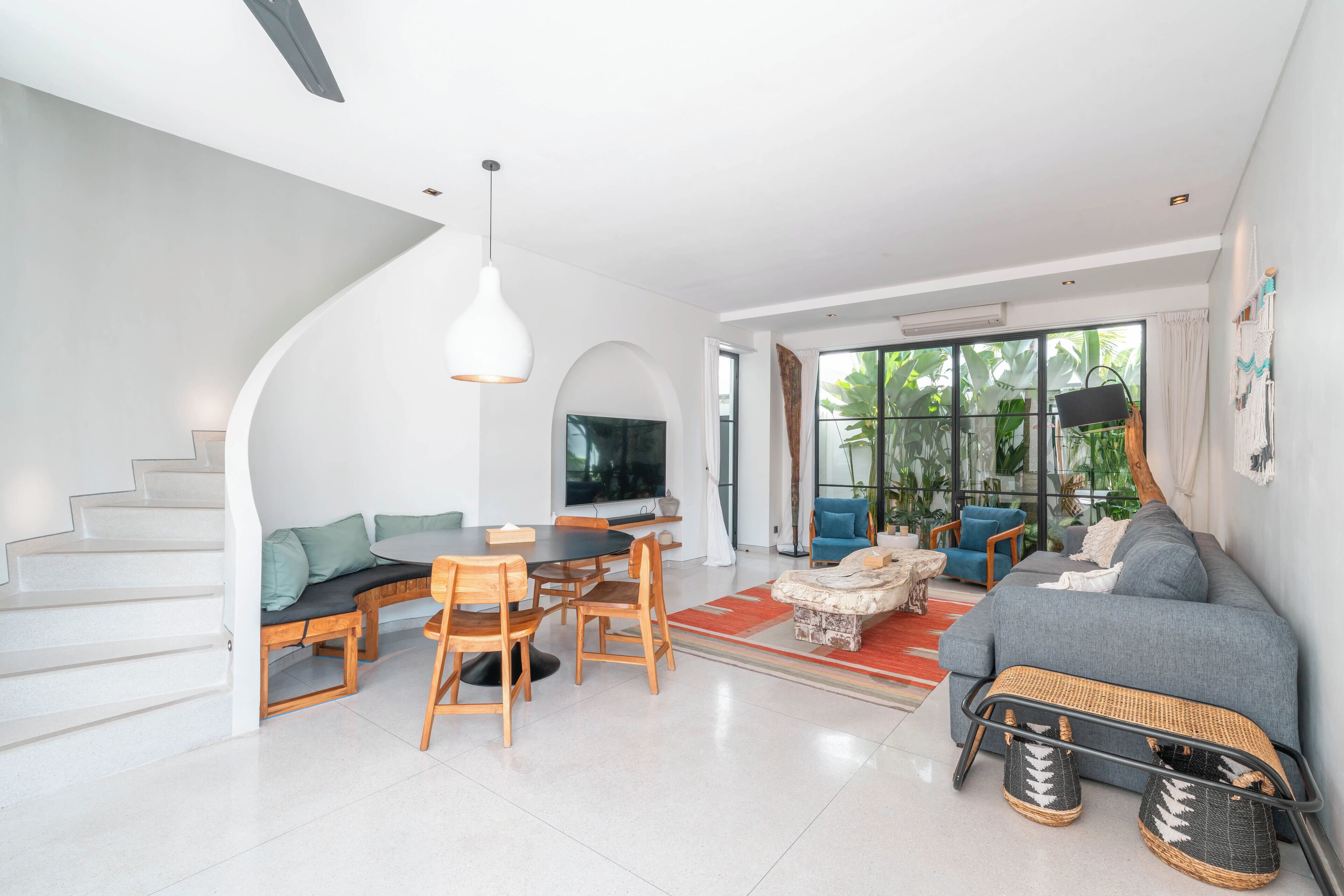 A modern living room with a staircase, a dining area, a sofa, and a TV.