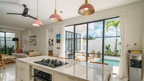 Una cocina moderna con una isla central, un ventilador de techo y grandes ventanales con vistas a una piscina.