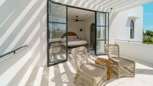 Un balcón moderno con mobiliario de mimbre, una cama con cabecera de madera y un ventilador de techo.