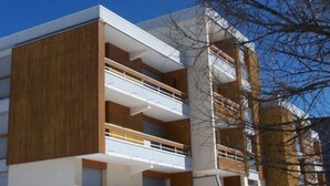 A modern multi-story building with a combination of wooden and white exterior panels, balconies, and a clear sky.