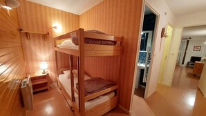 A bunk bed room with a wooden finish, a bedside table with a lamp, and a view of a bathroom through an open door.