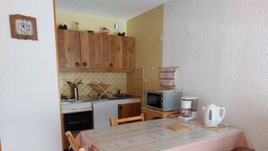 A compact kitchen with wooden cabinets, a microwave, a coffee maker, and a dining table with chairs.